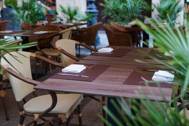 Etrafı yemyeşil bitkilerle çevrili düzgün düzenlenmiş masa ve sandalyelerle dolu bir açık hava yemek alanı.