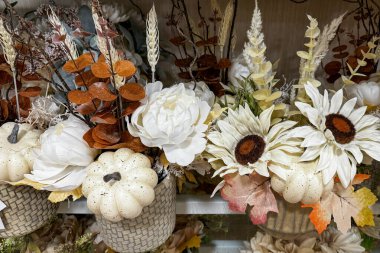 Beyaz balkabaklarının, yapay beyaz çiçeklerin, buğday saplarının ve kuru yaprakların yer aldığı sonbahar temalı dekoratif bir çiçek aranjmanı.
