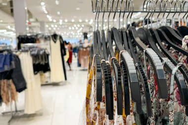 İçinde çeşitli elbiseler bulunan bir elbise askısı, parlak ışıklı bir perakende mağazasının içinde bulanık arka plan müşterileri ve ürünleri olan