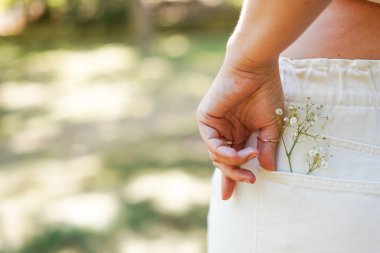 female hand on the back pocket of white pants, with a small sprig of delicate white flowers clipart