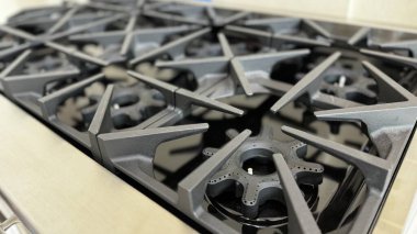 Gaz sobası siyah, demir ocakları keskin, açısal tasarım elementleri var.