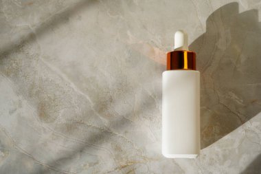 Kozmetik mat beyaz damla şişe desenli mermer bir yüzey üzerinde, yumuşak bir gölge döküyor