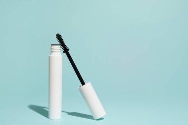 Beyaz rimel tüpü pastel mavi arka planda gösterilir, siyah asası aplikatörü göstermek için açılıdır.