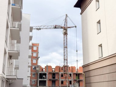 İki modern apartmanın arasına yerleştirilmiş uzun vinçli bir inşaat alanı.