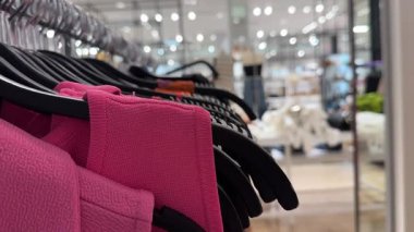 Modern, aydınlık bir giyim mağazasında siyah askılarda asılı parlak pembe elbiseler.