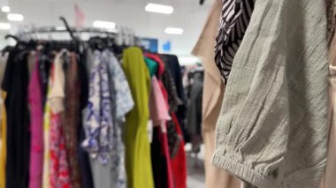 İyi aydınlatılmış bir mağazadaki elbise rafında çeşitli renkli elbiseler sergilenir. Bunlar arasında izler, desenler ve katı renkler de vardır.