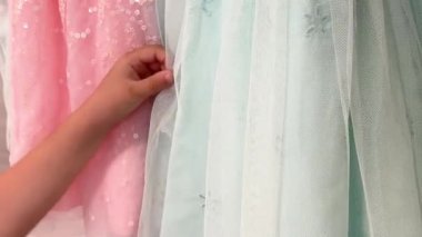 Bir çocuk nazikçe rengarenk tül elbiselere dokunur, biri pembeli, diğeri nane yeşili.