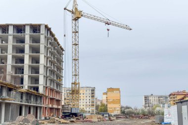 İnşaat alanında kısmen inşa edilmiş beton bir yapının yanında uzun bir vinç duruyor.