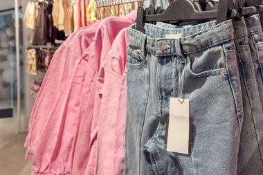 Bir giyim mağazasında pembe gömlekler ve etiketli mavi kot pantolon sergilenir