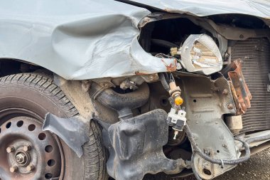 Hasarlı bir arabanın yakın çekiminde buruşmuş bir çamurluk, açığa çıkmış far parçaları ve çarpma sonrası bükülmüş metal parçaları görülüyor.
