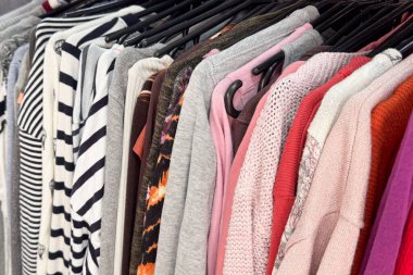 Gri, pembe, kırmızı tonlarda çizgilerden örgü örmeye kadar değişen renkli süveter ve üstler bir askıda sergilenir.