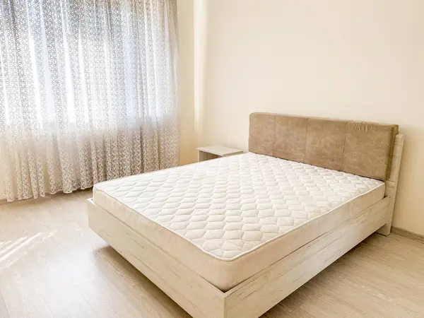 Yatak odasında çift kişilik yatak, yorgan, yumuşak yatak başlığı ve katıksız perdeler var.