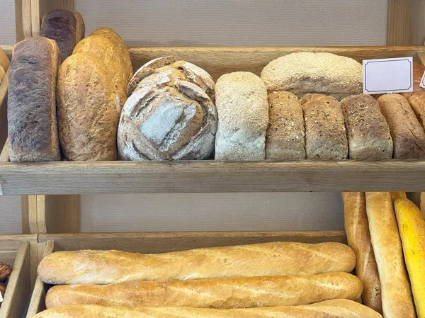 Ahşap bir fırın rafında yuvarlak, tohumlu ve kırsal somunlar da dahil olmak üzere çeşitli taze fırınlanmış ekmekler sergilenir.