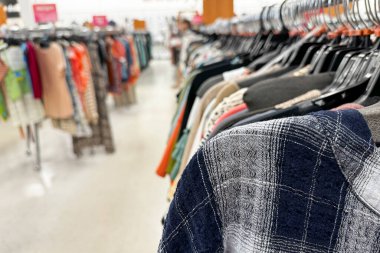 Parlak ışıklı bir perakende mağazasında askılarda çeşitli giysiler bulunan elbise raflarının yakın çekim görüntüsü