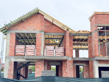 Kısmen inşa edilmiş tuğla bir ev açıkta duran ahşap kirişler ve beton desteklerle ayakta duruyor.