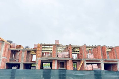 Kısmen inşa edilmiş tuğla bir ev açıkta duran ahşap kirişler ve beton desteklerle ayakta duruyor.