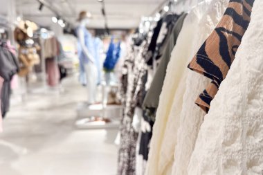 Renkli giysilerle dolu bir elbise rafı parlak bir moda mağazasının ön planında belirgin bir şekilde sergileniyor.