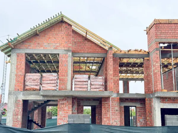 Kısmen inşa edilmiş tuğla bir ev açıkta duran ahşap kirişler ve beton desteklerle ayakta duruyor.