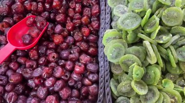 Sol tarafta bir kutu parlak kırmızı kurutulmuş kiraz ve sağ tarafta canlı yeşil kurutulmuş kivi dilimleri.