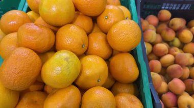 Taze, parlak portakallarla dolu bir sandık bir markette olgun kayısıların yanında duruyor.