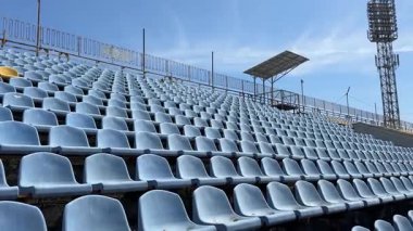 Boş mavi plastik stadyum koltukları parlak bir gökyüzünün altında, tek bir sarı koltuk tek sıra halinde duruyor.