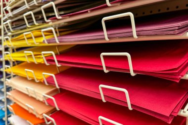 Sanat malzemeleri satan bir mağazanın metal rafında düzgünce düzenlenmiş renkli el işi kağıtları.