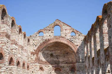 Kemerli camları ve kısmen çökmüş çatısı olan eski bir taş ve tuğla kalıntısı berrak mavi bir gökyüzünün altında duruyor.