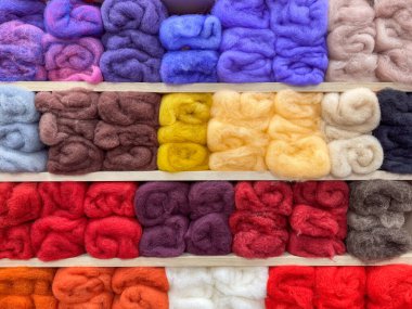 Ahşap raflarda düzgünce sergilenen farklı tonlarda gezen renkli yün yığınları