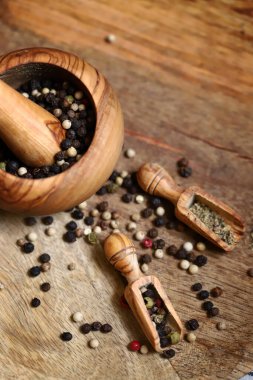 Mix of peppercorns in a wooden mortar and wooden spatulas.
