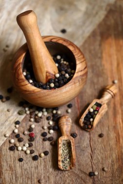 Mix of peppercorns in a wooden mortar and wooden spatulas.