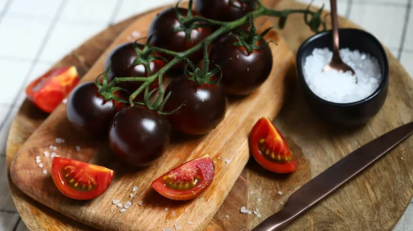 Black tomatoes with sea salt on a wooden board.