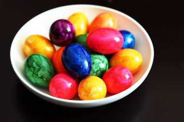 Siyah arka planda beyaz tabakta renkli yumurtalar..