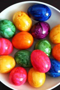 Siyah arka planda beyaz tabakta renkli yumurtalar..