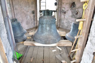 Metalden yapılmış üç çan, bir binanın ahşap zemininde duruyor. Onlar idiyofon ve kilise çanları, ghantalar ya da gazlı müzik aletleri olabilir.