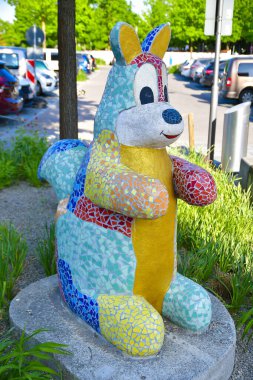 Canlı yeşil bir kanguru heykeli boks eldiveni takıyor ve halka açık alana bir parça sanat katıyor. Heykel, yemyeşil çimenler ve bitki yaşamlarıyla çevrili mavi bir tekerleğin üzerinde duruyor.