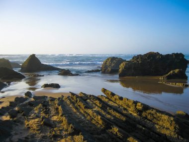 Alacakaranlıkta gökyüzünün altında, kıyı ve okyanus şekilli dağlık arazide kayalarla süslenmiş güzel bir su kütlesine sahip doğal bir manzara.