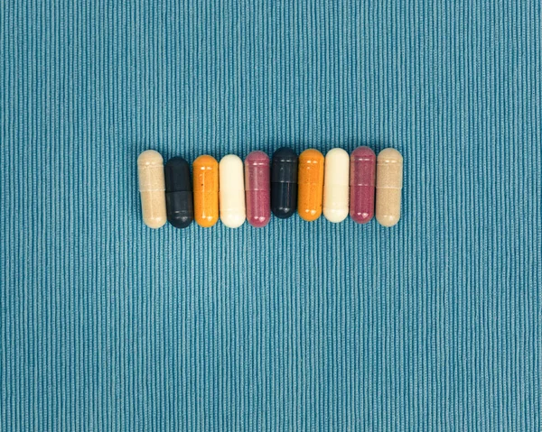 Top view of a variety of vitamin and mineral supplements in capsules. Multicolored pills in orange and red on blue textured background.