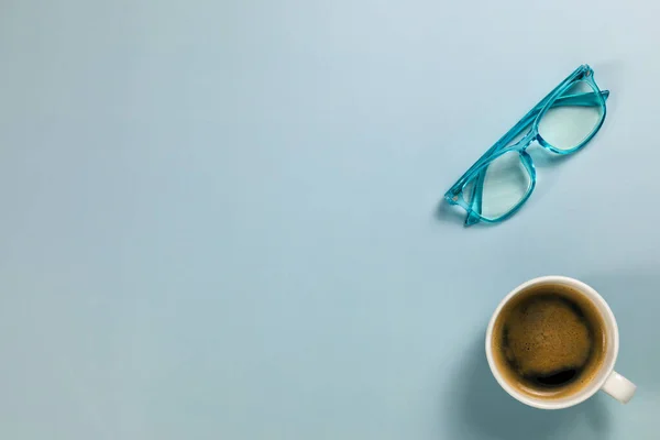 Sabah kahvesi fincanı ve bir çift mavi okuma gözlüğü.