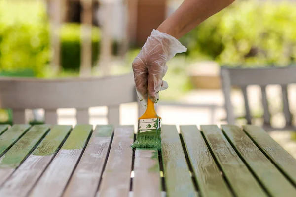 Painting Table with brush in protective gloves. Worker Paints garden Wood furniture in green. Renewing, Renovation Wooden Garden Furniture