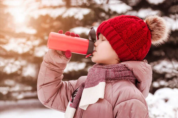 Thermos Mug for Children in Cold Winter. Girl Child Teen  Drinking Hot Tea in Thermos mug in Winter Walking with Snow Outdoors.
