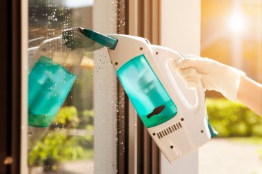 Cleaning Window Glass with Electrical Device. Close up of Woman's Gloved hand Washing Window with Electro Machine