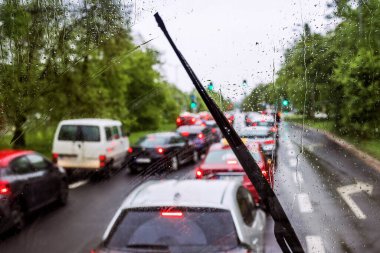 Trafik sıkışıklığında araba kullanmak, ön camda yağmur damlaları, cam silecekler, trafik ışıkları. Araba penceresine yağmur damlası.
