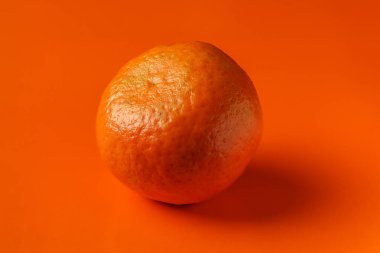 Mandarin with shadow on orange background, close-up