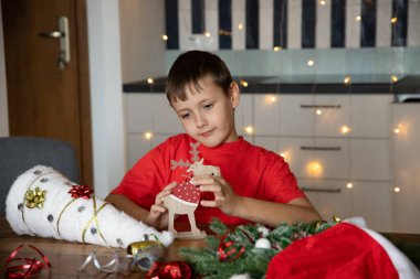 Kırmızı tişörtlü şirin bir çocuk kendi başına Noel zanaatı yapıyor. Yeni yıl. El yapımı iş. ÇEVİR