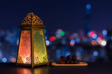 Lantern and small plate of dates fruit with night sky and city bokeh light background for the Muslim feast of the holy month of Ramadan Kareem. clipart