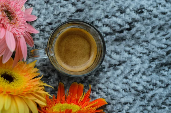 stock image A glass of Espresso coffee shot puts on bed with Gerbera flowers. Stay home concept.