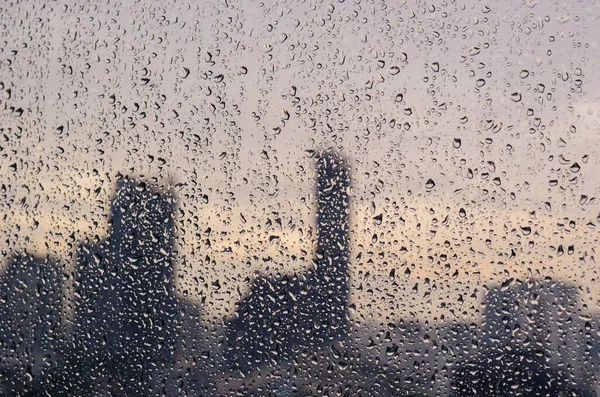 モンスーンの季節のガラス窓に雨が降る 明るい街の建物の背景と夕暮れの時間 — ストック写真