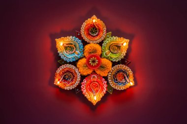 Diwali festivali için kırmızı zemin üzerinde turuncu kadife çiçekleri bulunan dekoratif kil diya lambaları.