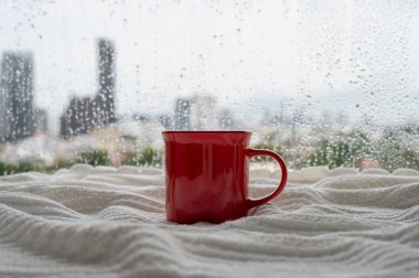 Pencereye yağmur düştüğünde kırmızı bir fincan kahve battaniyeye sarınır. Evde kal ve konsepti rahatlat..