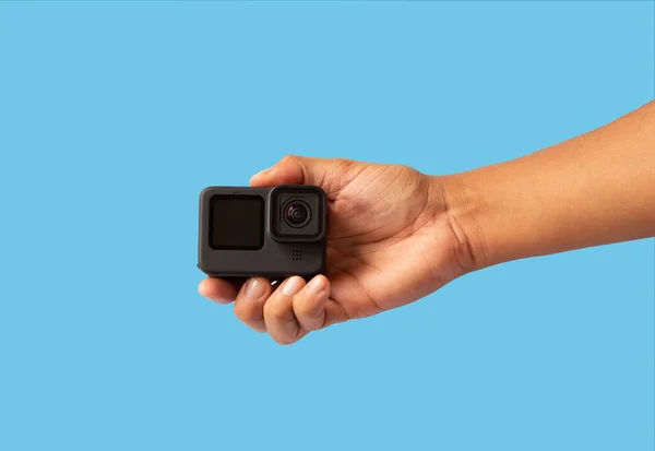 a man\'s hand holding an action camera on blue background